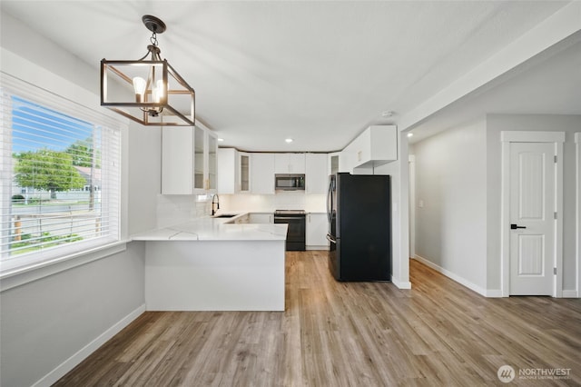 kitchen with white cabinets, black appliances, a sink, baseboards, and a peninsula