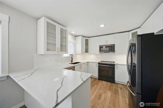 kitchen featuring black electric range oven, a sink, freestanding refrigerator, light stone countertops, and a peninsula