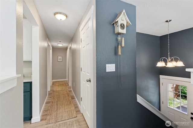 hall with a chandelier, light wood-style flooring, and baseboards
