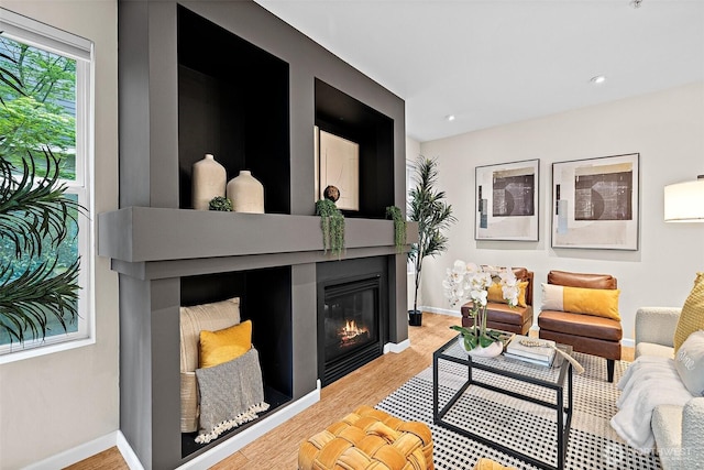 living room featuring baseboards, recessed lighting, a glass covered fireplace, and wood finished floors