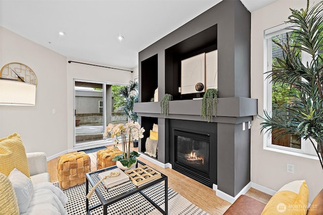 living room with baseboards, recessed lighting, a glass covered fireplace, and wood finished floors