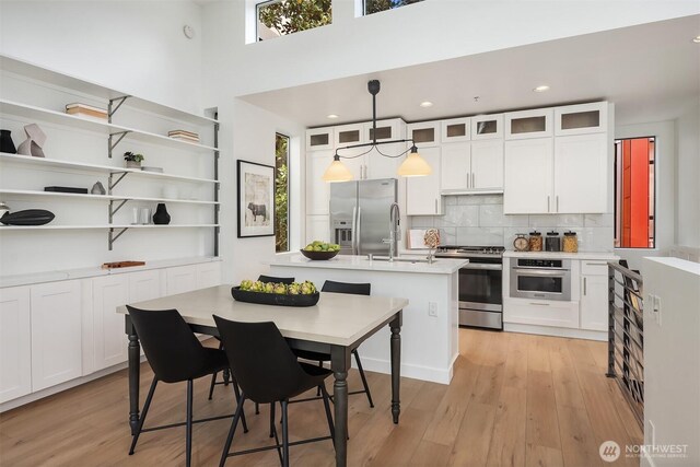 kitchen featuring a healthy amount of sunlight, a kitchen island with sink, appliances with stainless steel finishes, a sink, and light countertops