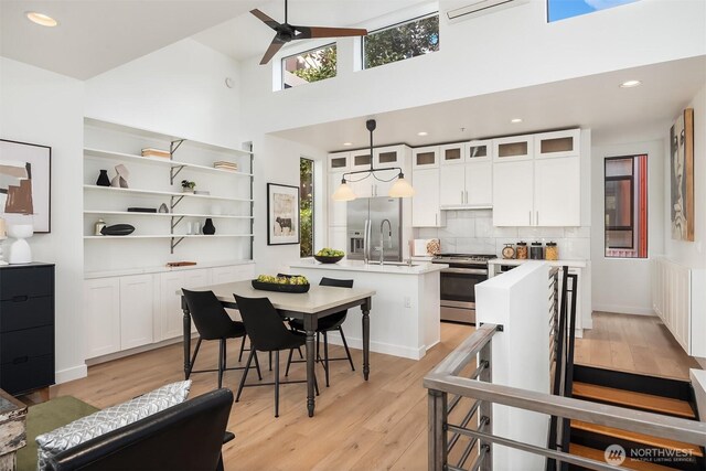 kitchen with a high ceiling, light wood finished floors, a kitchen island with sink, and gas range