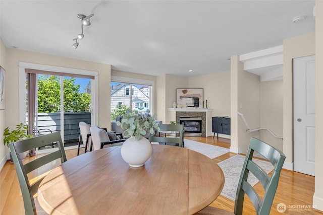 dining room featuring light wood-type flooring, baseboards, a glass covered fireplace, and a wealth of natural light