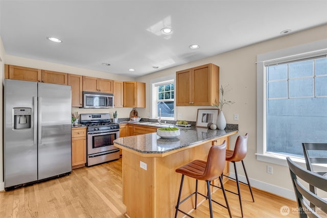 kitchen with a peninsula, dark stone countertops, light wood-style floors, a breakfast bar, and stainless steel appliances