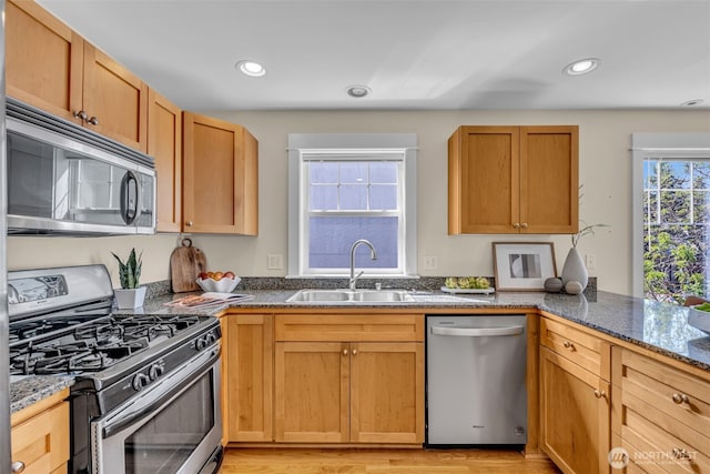 kitchen with a sink, appliances with stainless steel finishes, light wood-style floors, and dark stone counters