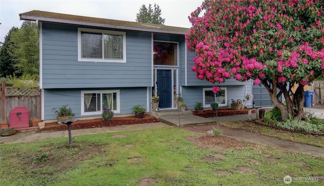 raised ranch featuring a front lawn and fence