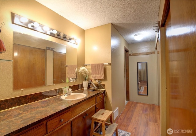 bathroom with a textured ceiling, visible vents, wood finished floors, and vanity