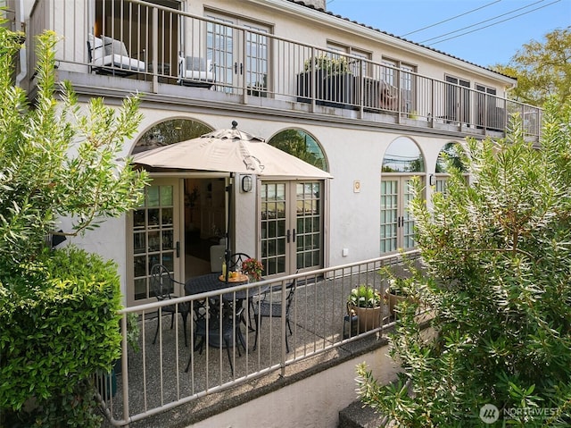 rear view of house with french doors, stucco siding, and a balcony