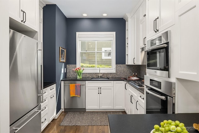 kitchen featuring white cabinets, dark countertops, appliances with stainless steel finishes, a sink, and backsplash