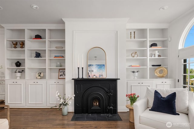 living area featuring crown molding, a fireplace with flush hearth, dark wood-style flooring, and built in shelves