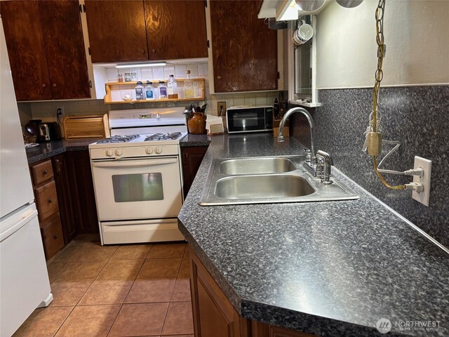 kitchen with white appliances, tile patterned flooring, decorative backsplash, dark countertops, and a sink