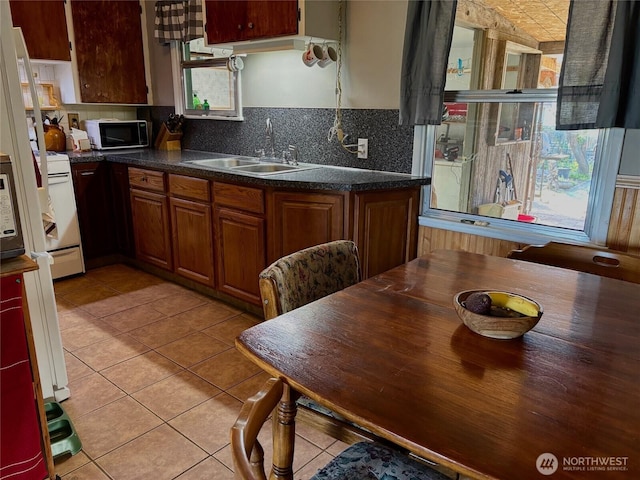 kitchen featuring decorative backsplash, light tile patterned floors, dark countertops, a sink, and black microwave