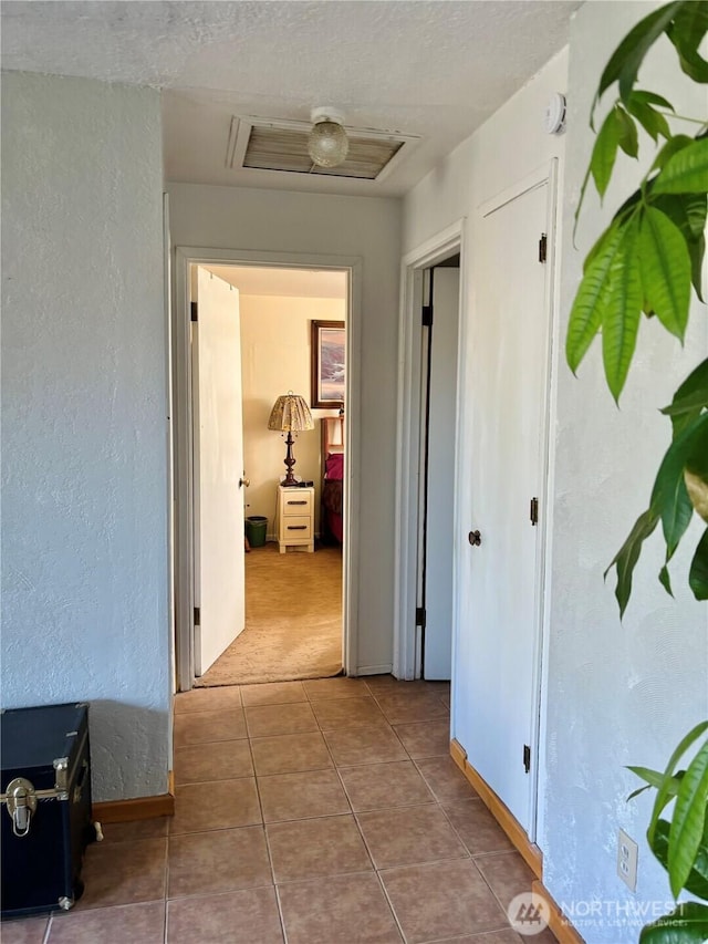hall featuring carpet flooring, tile patterned flooring, visible vents, and a textured wall