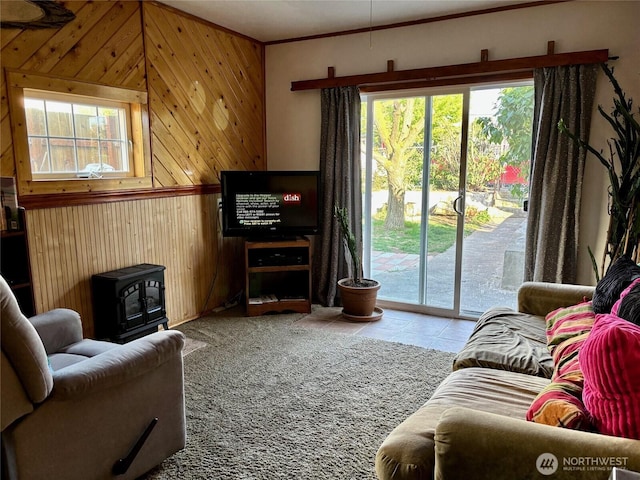 tiled living room featuring a wood stove, a healthy amount of sunlight, and wooden walls