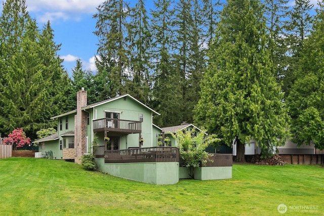 rear view of property featuring a chimney, a yard, and a balcony