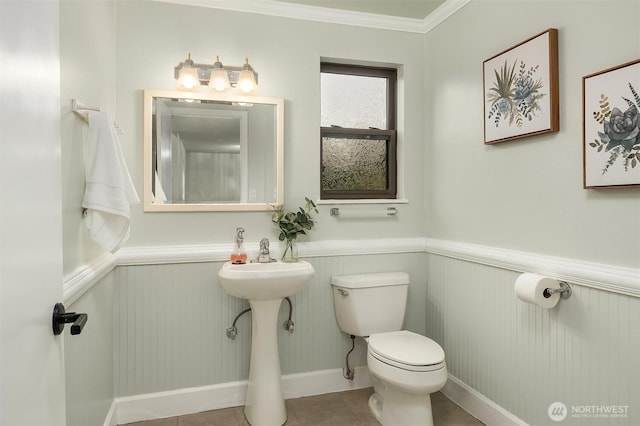 half bathroom with crown molding, wainscoting, tile patterned floors, baseboards, and toilet