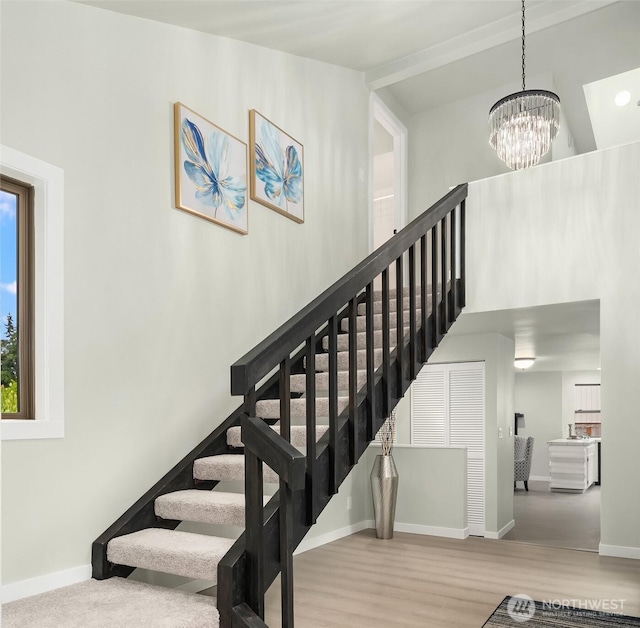 stairway with baseboards, wood finished floors, and a notable chandelier