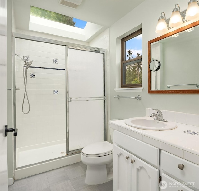 bathroom with visible vents, vanity, toilet, a shower stall, and a skylight