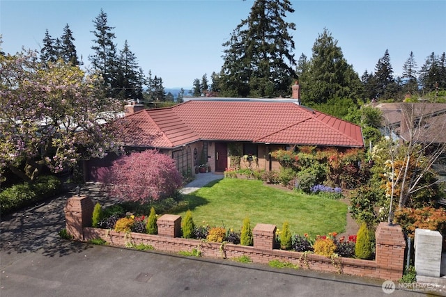 view of front facade with a front yard, a tiled roof, and a chimney