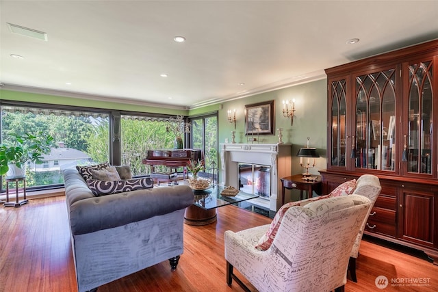 living area with visible vents, wood finished floors, a glass covered fireplace, ornamental molding, and recessed lighting