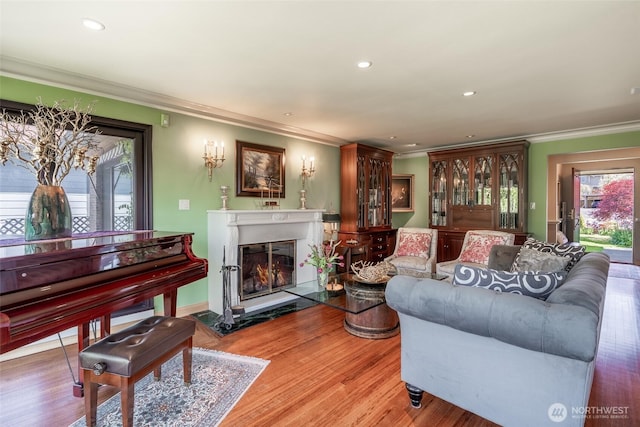 living area with crown molding, a glass covered fireplace, recessed lighting, and a healthy amount of sunlight