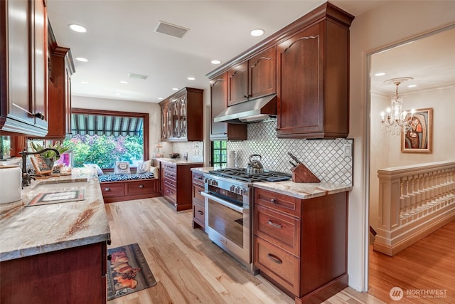 kitchen with backsplash, high end range, light wood finished floors, under cabinet range hood, and recessed lighting