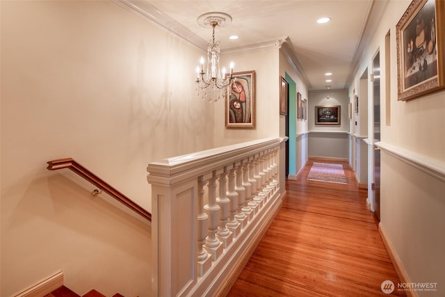 hallway with ornamental molding, wood finished floors, recessed lighting, a notable chandelier, and an upstairs landing