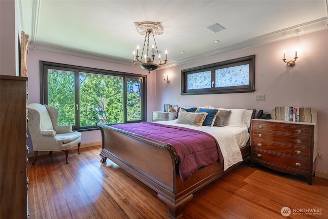 bedroom with an inviting chandelier, ornamental molding, visible vents, wood finished floors, and baseboards