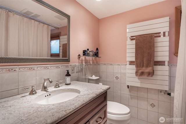 full bath with visible vents, tile walls, a wainscoted wall, vanity, and toilet