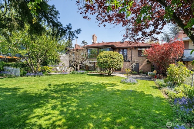 rear view of property featuring a tiled roof, a chimney, a lawn, fence, and a patio