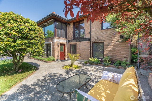 exterior space with brick siding, a patio area, and a balcony