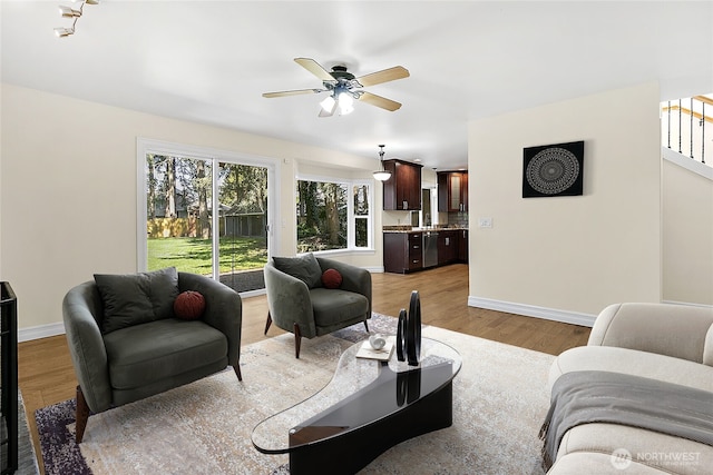 living area with light wood-style floors, baseboards, stairway, and a ceiling fan