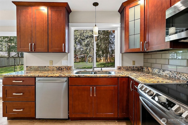 kitchen with appliances with stainless steel finishes, a sink, dark stone counters, pendant lighting, and glass insert cabinets