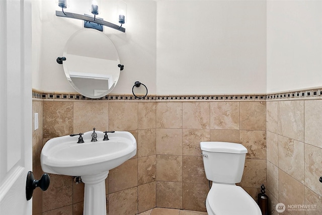 bathroom with wainscoting, toilet, and tile walls