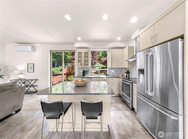 kitchen with stainless steel appliances, wall chimney exhaust hood, a breakfast bar area, a wall mounted air conditioner, and a center island