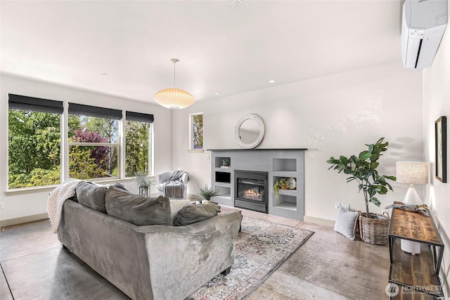 living area with a wall mounted AC, concrete flooring, a glass covered fireplace, baseboards, and recessed lighting