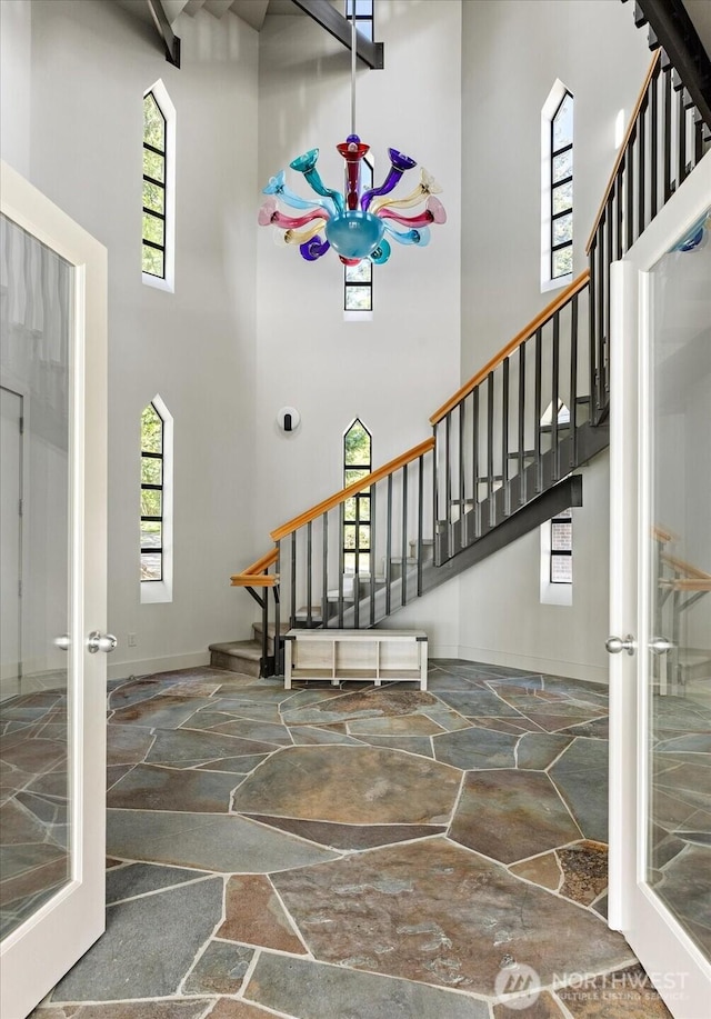 entryway featuring french doors, a towering ceiling, stone floors, and stairway