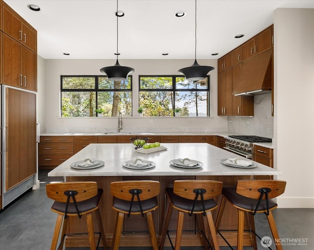 kitchen with brown cabinets, a sink, light countertops, premium range hood, and high end appliances