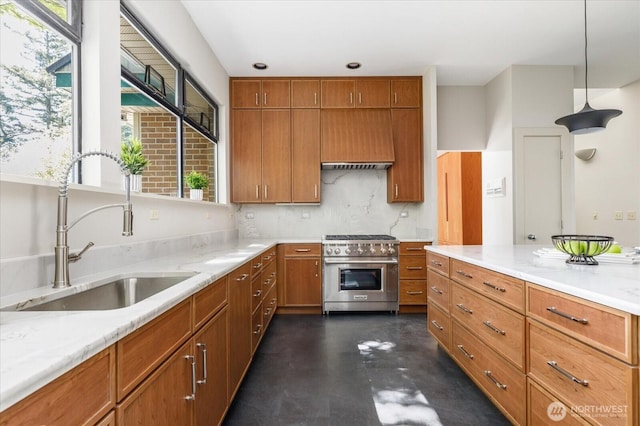 kitchen featuring custom exhaust hood, stainless steel stove, brown cabinets, light stone counters, and a sink