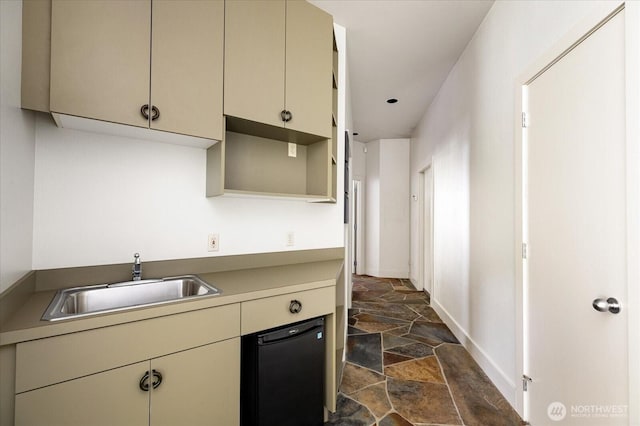 kitchen with baseboards, a sink, stone finish flooring, and cream cabinetry