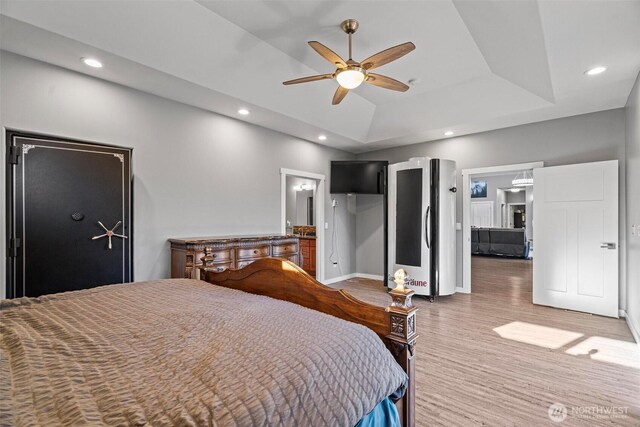 bedroom with baseboards, light wood-style floors, ensuite bathroom, a tray ceiling, and recessed lighting