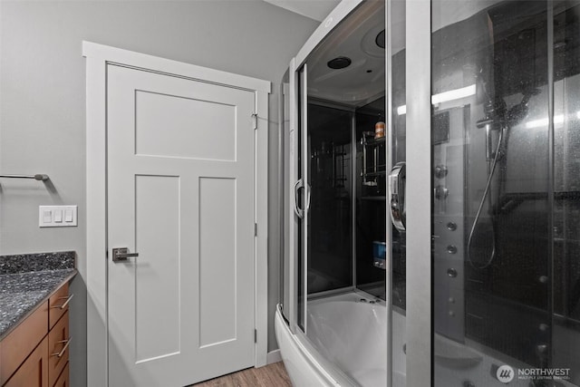 full bathroom featuring a shower with door, wood finished floors, and vanity