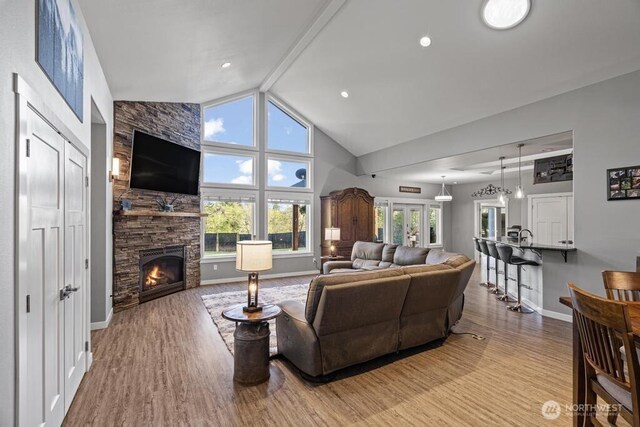 living area with baseboards, a fireplace, high vaulted ceiling, and wood finished floors