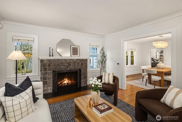 living room featuring wood finished floors, baseboards, a warm lit fireplace, a chandelier, and ornamental molding