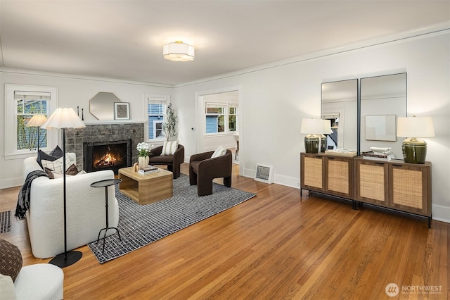 living area with baseboards, a lit fireplace, wood finished floors, and visible vents