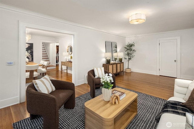 living area with baseboards, ornamental molding, wood finished floors, and stairway