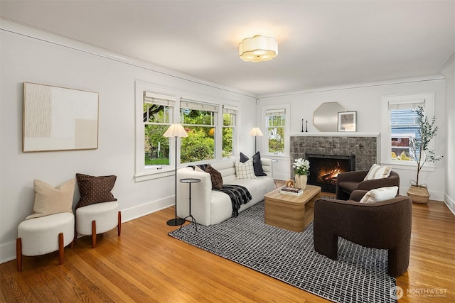 living room featuring a healthy amount of sunlight, baseboards, light wood-type flooring, and a warm lit fireplace