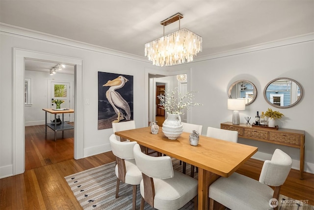 dining space featuring crown molding, baseboards, a notable chandelier, and wood finished floors