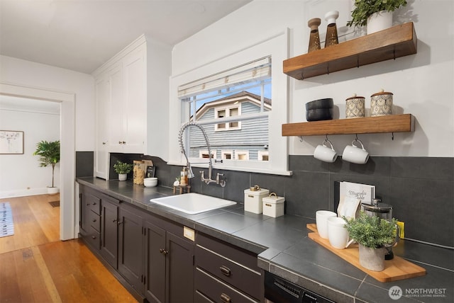 kitchen featuring tile countertops, open shelves, a sink, light wood finished floors, and white cabinetry